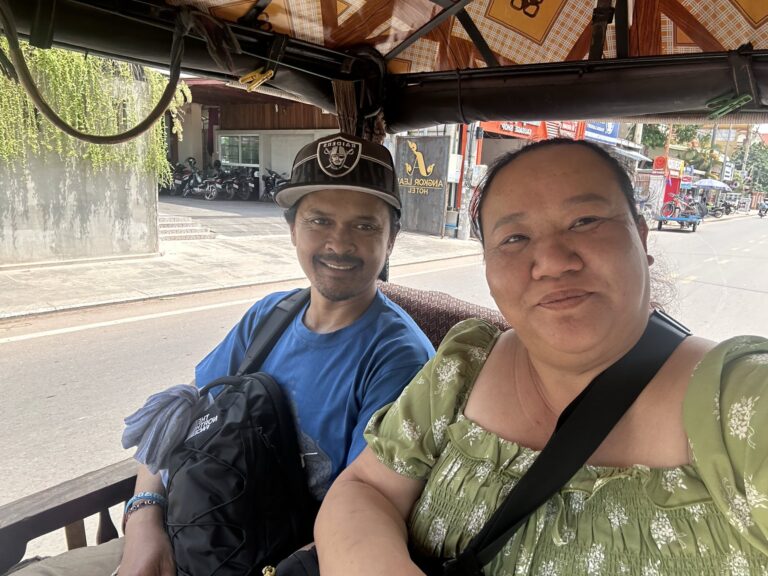 A man wearing a blue t-shirt and a hat sitting next to a woman with a green top sitting in a tuk tuk in Cambodia.
