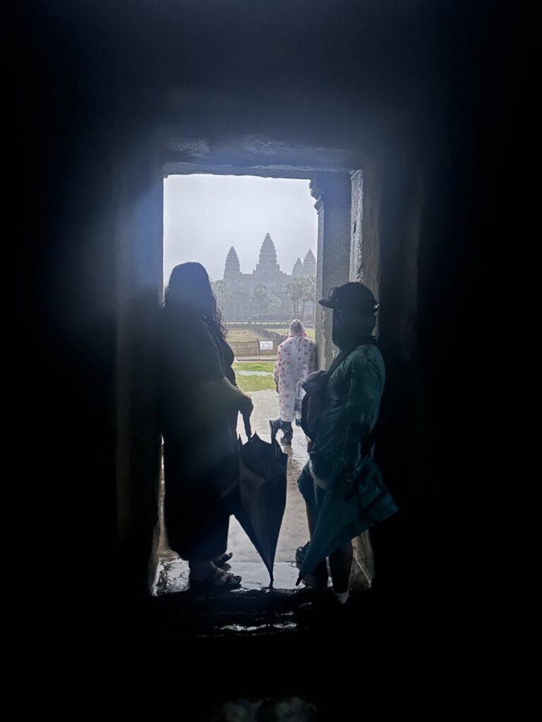 A man and a woman who's carrying an umbrella standing in building looking outside at the temples of Angkor Wat in Siem Reap Cambodia.