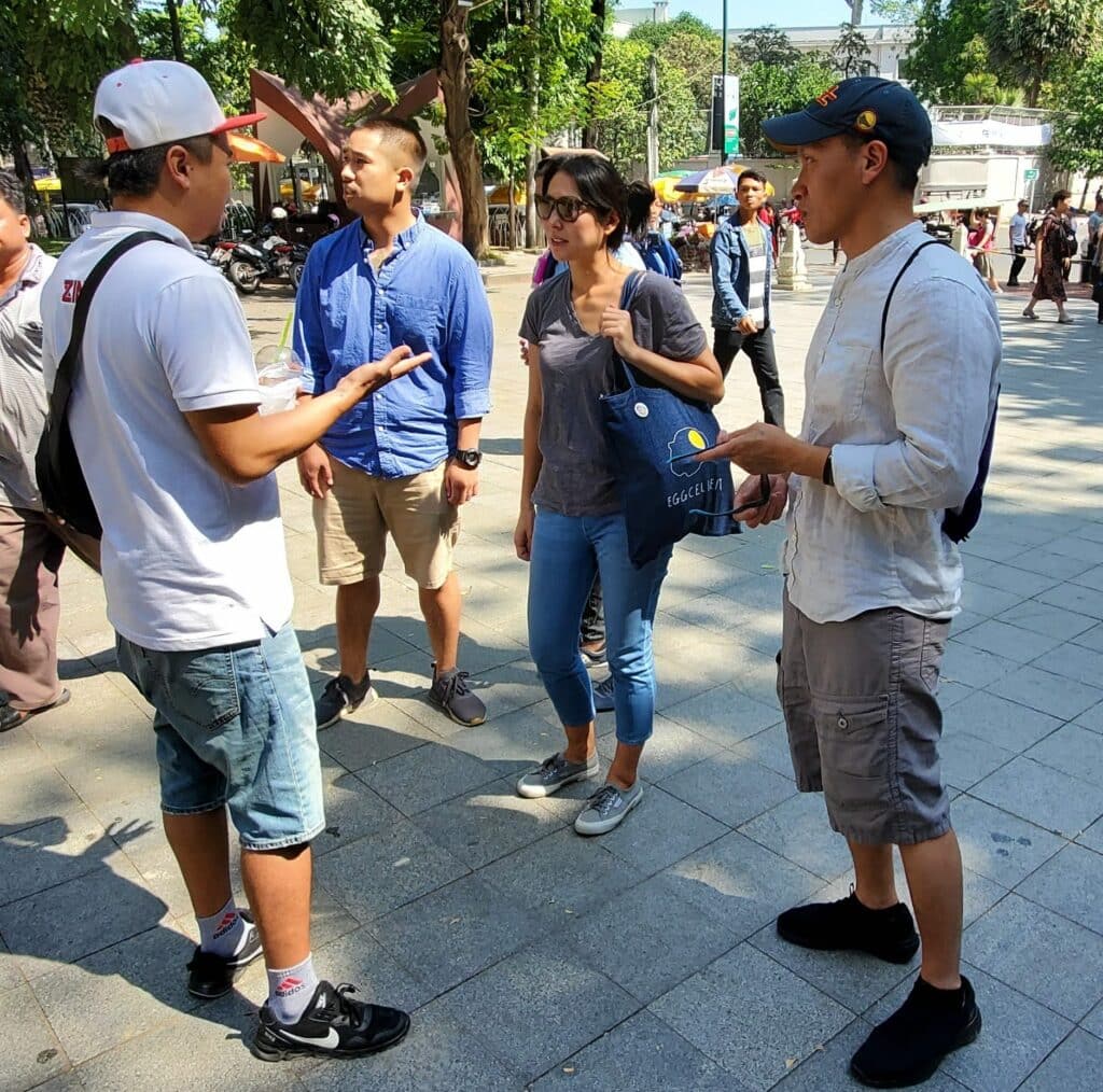 Two men a woman listening to a man with a baseball cap talking.